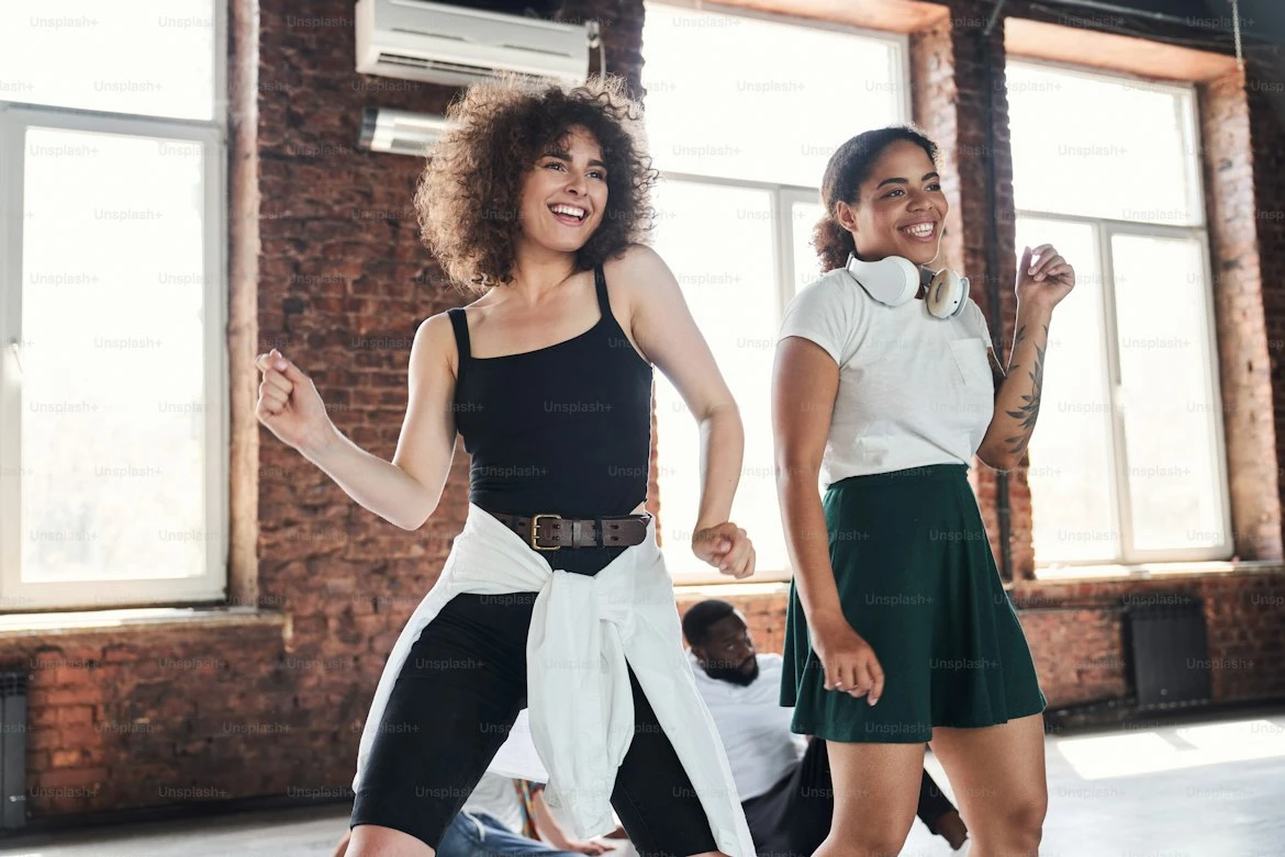 Two smiling dancers in a brick-walled studio