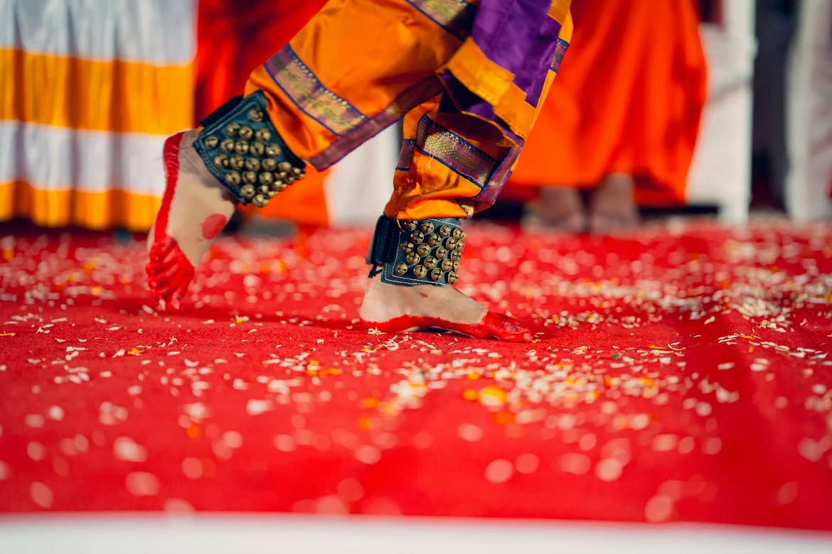 Close-up of a dancer in ankle bells on a red floor scattered with petals